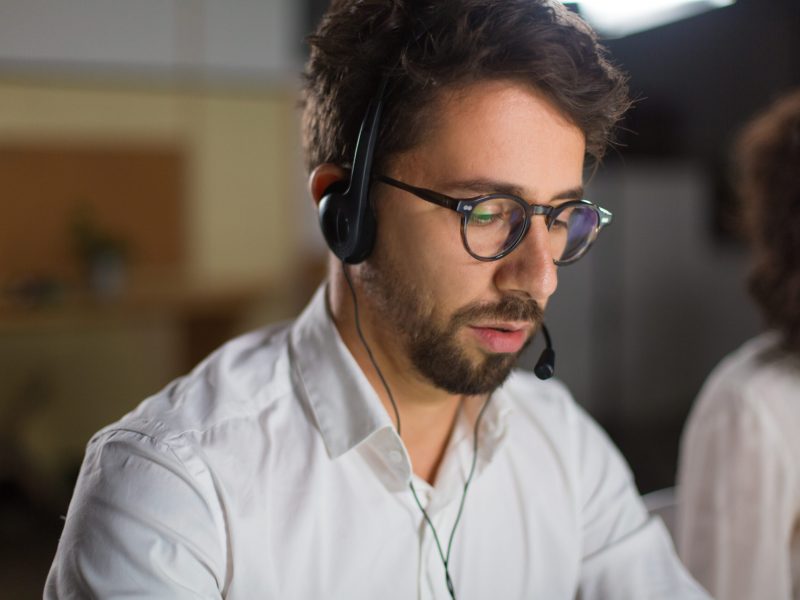 Closeup shot of confident call center operator. Handsome young man with headset looking down. Call center concept
