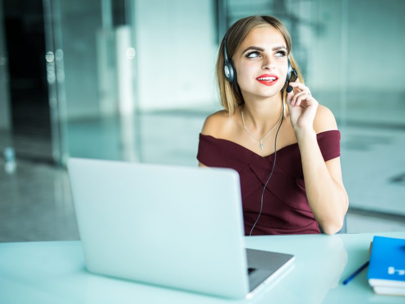 Focused attentive woman in headphones sits at desk with laptop, looks at screen, makes notes, learns foreign language in internet, online study course self-education on web consults client by video
